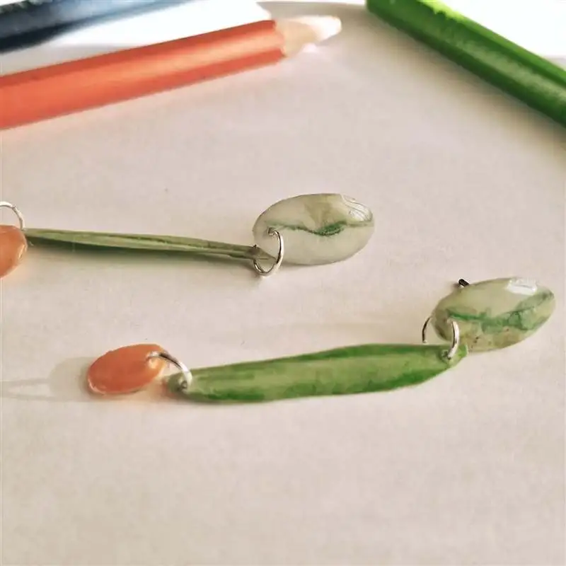 Pendientes de resina en verde y coral junto a lápices de colores, pieza hecha a mano en un taller de joyería en Barcelona