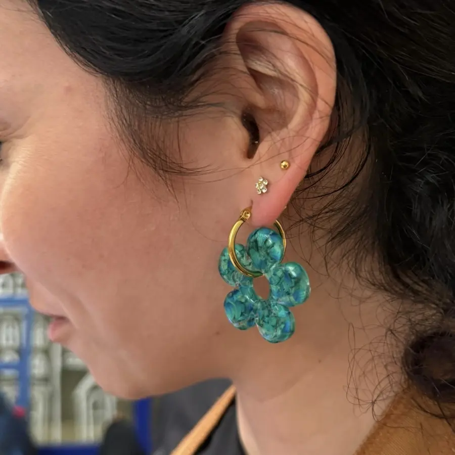 Blue and green resin flower earring with a gold hoop, worn on the ear